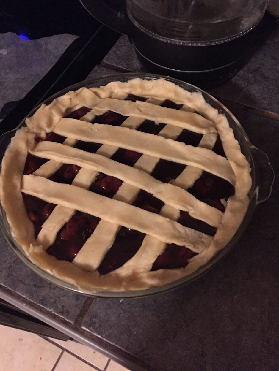 The top crust is applied to an uncooked cherry pie.