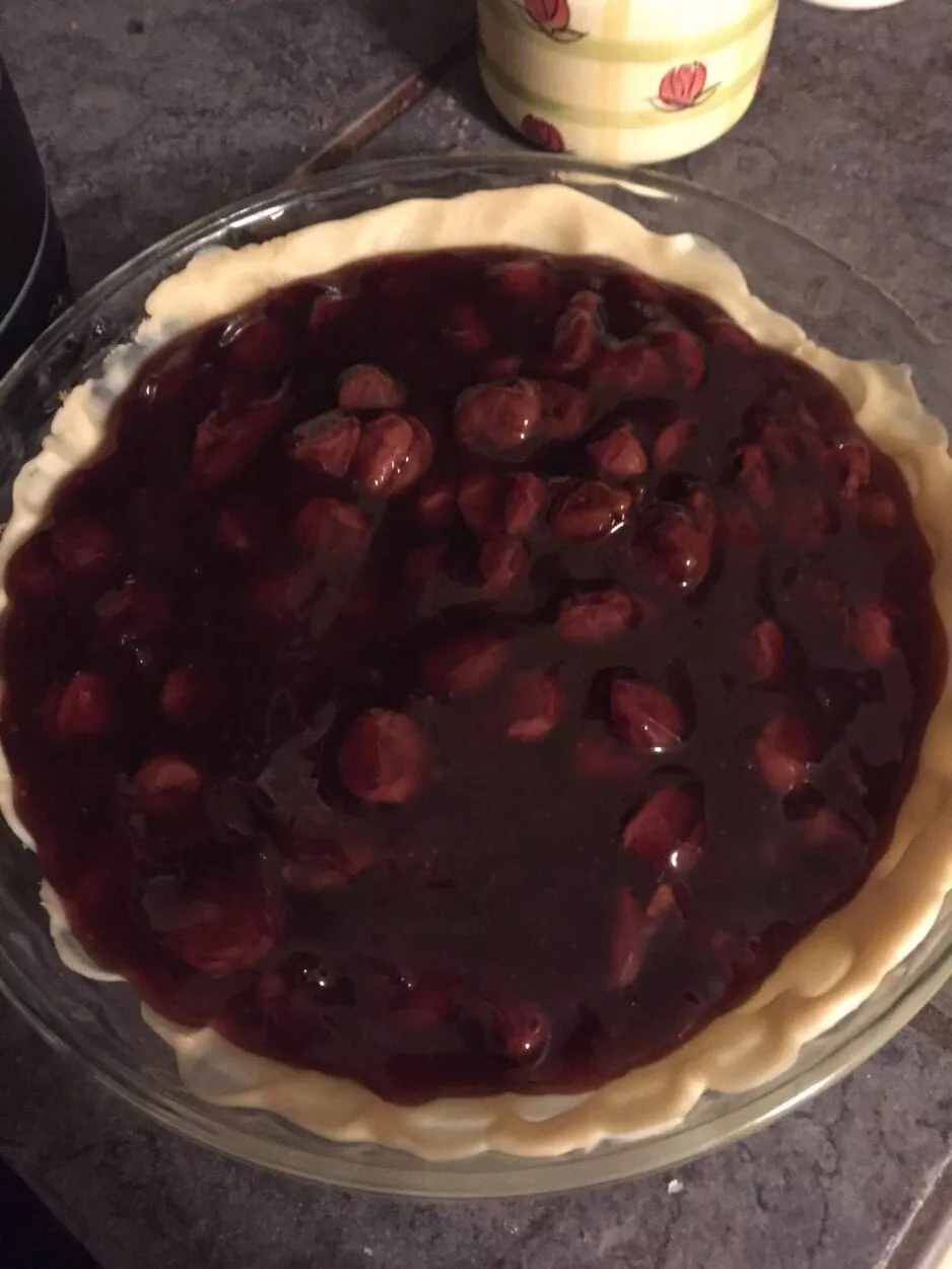 Cherries on top of pie crust in its dish, in the bowl ready for top crust to be applied.