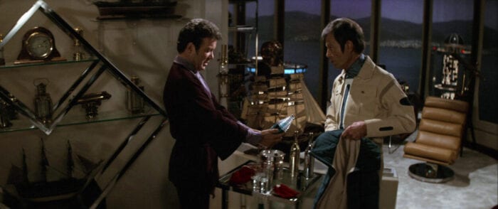 Kirk holds a bottle of Romulan Ale while McCoy looks on