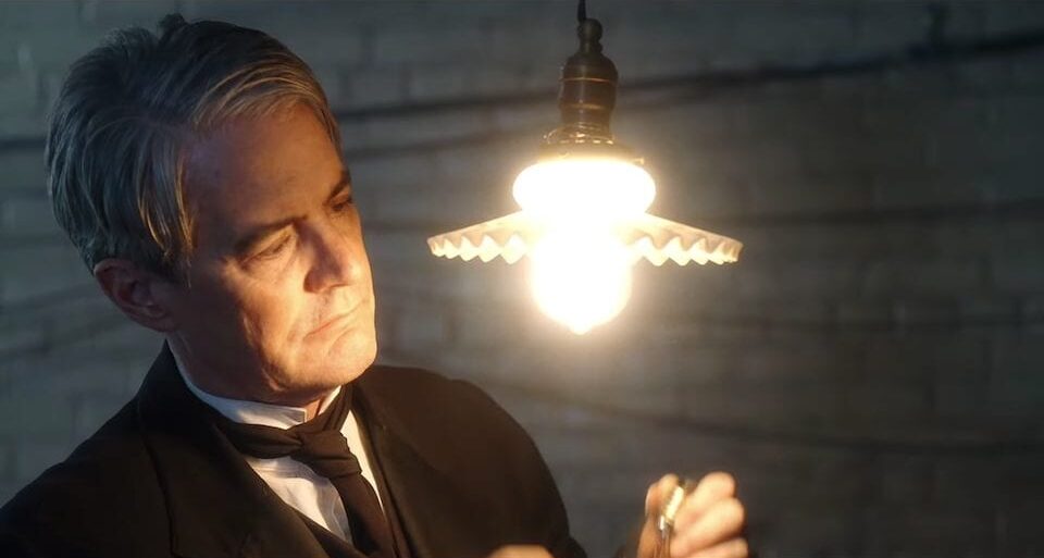 Thomas Edison (Kyle MacLachlan) inspects a lit-up lightbulb that he just installed.