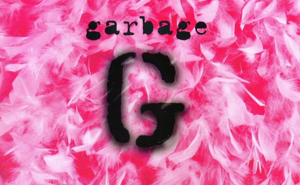 Cutouts of a letter G are spraypainted and are on top of a pink background littered with white feathers.