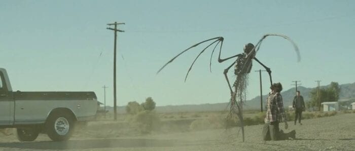 A bizarre demon shoves its arm down a man's throat on a desert road