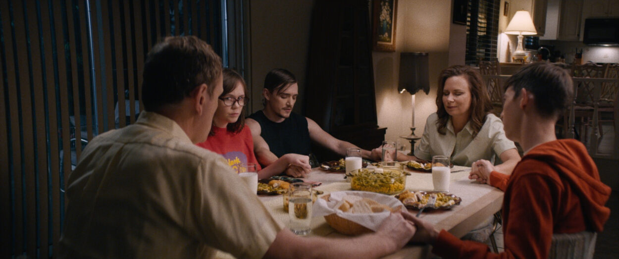 Patty (Emily Skeggs), Simon (Kyle Gallner), Connie (Mary Lynn Rajskub) and family all hold hands around the dinner table in prayer.