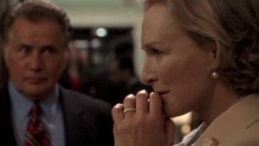 Glenn Close as Evelyn Baker Lang in The Supremes stands with her hands to her mouth deep in thought as President Bartlet stands out of focus to the right.