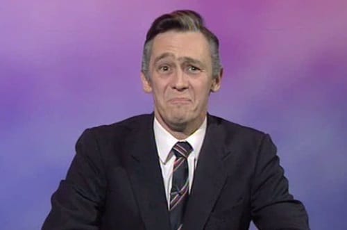 Paul Whitehouse smirks in front of a purple news background