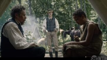 A shocked John Brown (Ethan Hawke) sitting inside a tent to the left and Henry "Little Onion" Shackleford (Joshua Caleb Johnson)making a terrible face after taking a bite from an onion sitting to the right while John Brown Jr. stands in the center between them with cups in his hands.