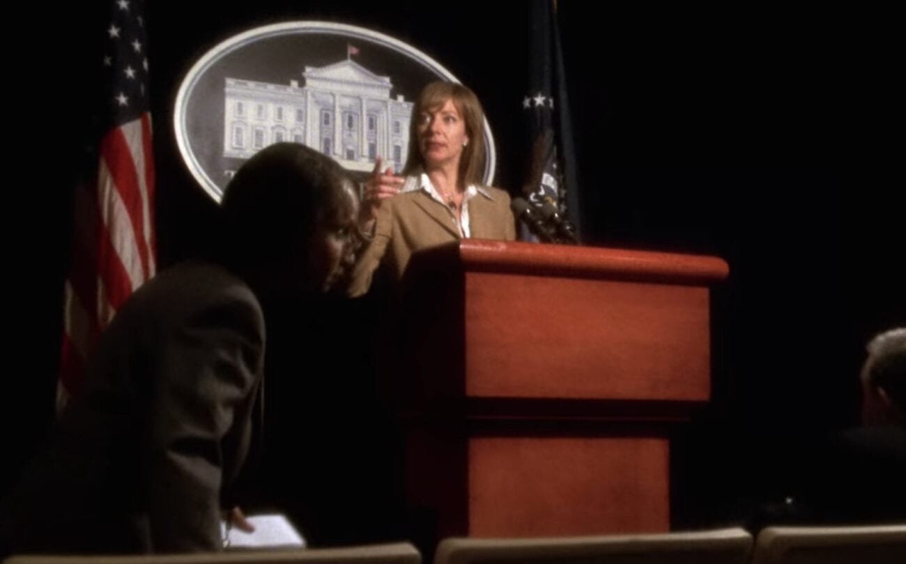 CJ looks to the side with a finger in the air as she stands behind a podium
