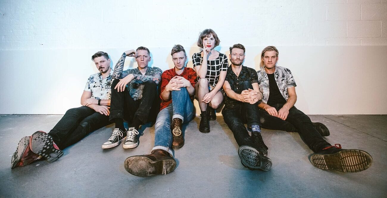 The six member of the band Skinny Lister sitting on the floor looking into the camera