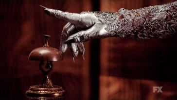 A silver hand with long nails reaches for a bell