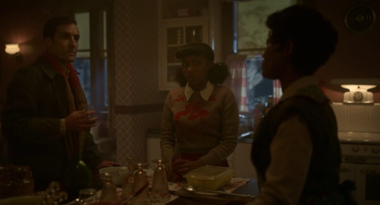 Thurman Smutney holds a drink in celebration in the family kitchen while Ethelrida nervously looks at Dibella, who is looking back disappointedly at Thurman.