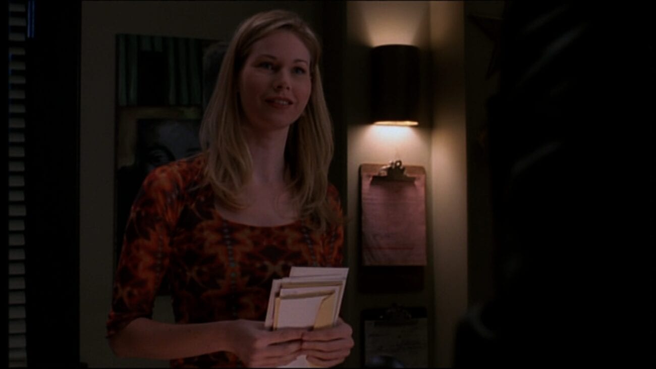 Anne stands behind her desk in the shelter's office, holding a stack of letters and smiling at Angel