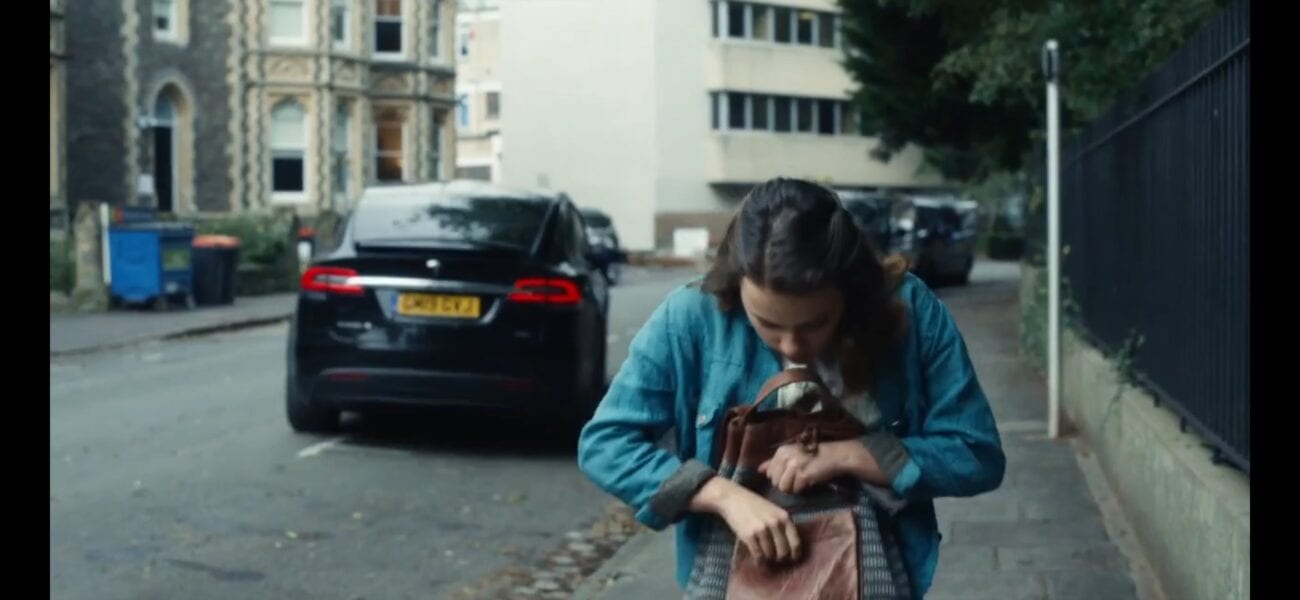 His Dark Materials - Lyra looks in her satchel as a car drives away behind her