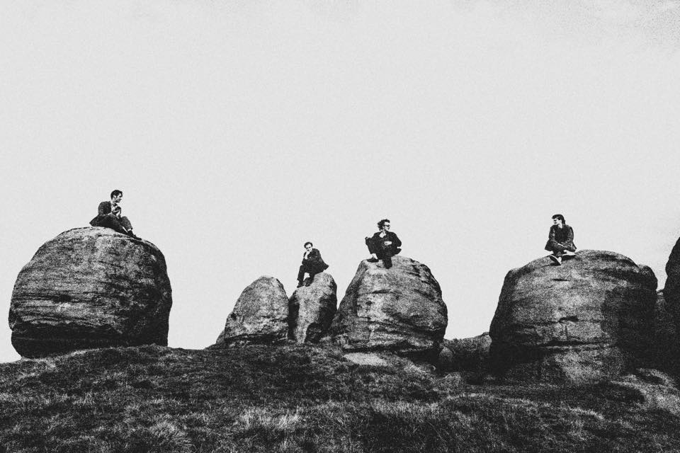 Black and white photo of the four male members of The Lounge Society, each sitting on a rock