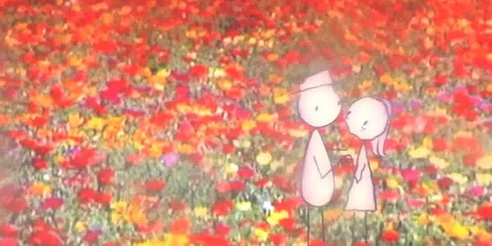 Bill, a stick man with an oval-shaped body and a hat holding hands with and gently caressing the face of an older looking stick woman with long hair and a dress. They are standing in front of a field of red, orange, yellow, and pink flowers.