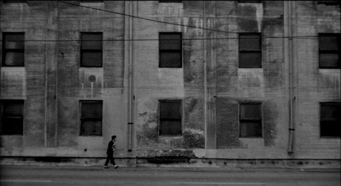 Henry (Jack Nance) walks by himself past a dilapidated factory.