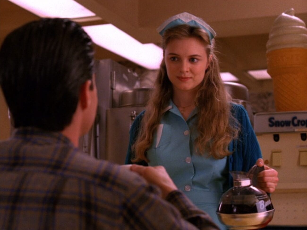 Annie in her waitress uniform stands before Cooper in plaid, holding a coffee pot 