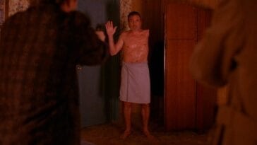 The one-armed man raises his hand while dressed in a towel