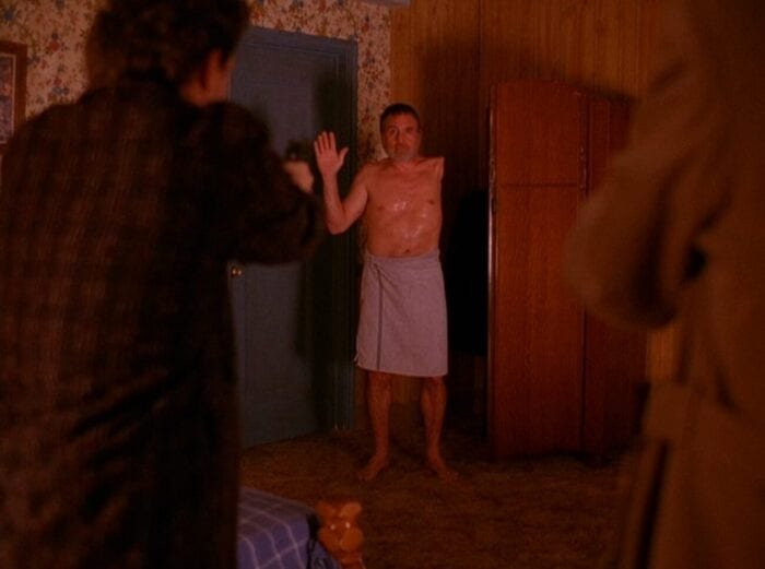 The one-armed man raises his hand while dressed in a towel