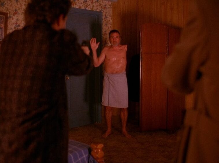 The one-armed man raises his hand while dressed in a towel