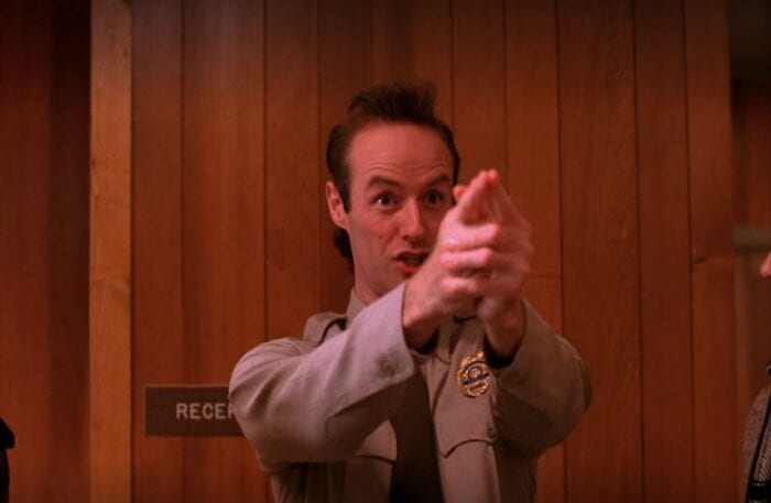 Andy points his fingers in front of him to make a pretend gun as he stands in the Sheriff's station in Twin Peaks
