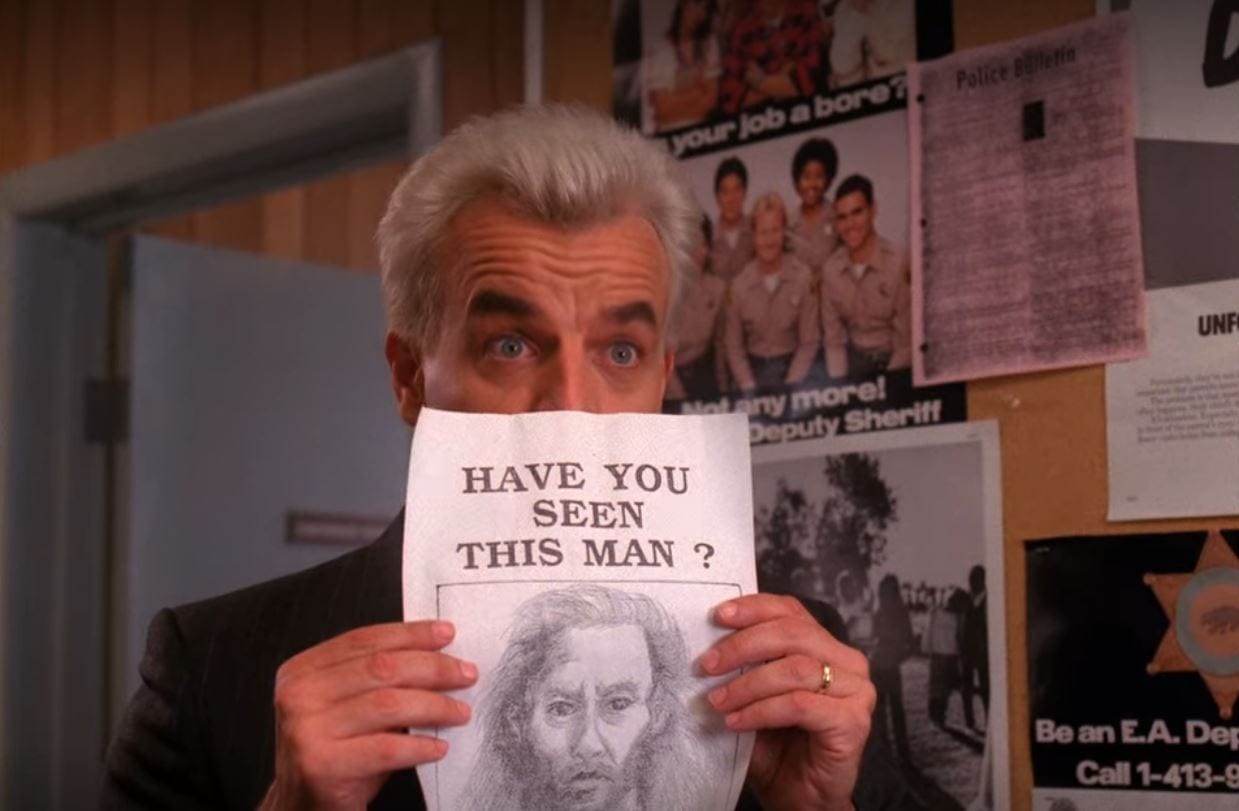 Leland holds a drawing of BOB up, obscuring the lower half of his own face, as he stands in front of a bulletin board in the Twin Peaks Sheriff's station