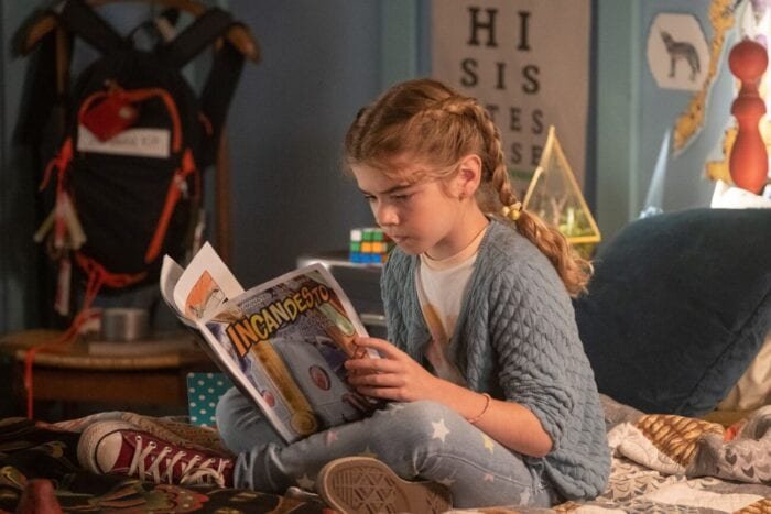 Flora reads her father's comic book on her bed.