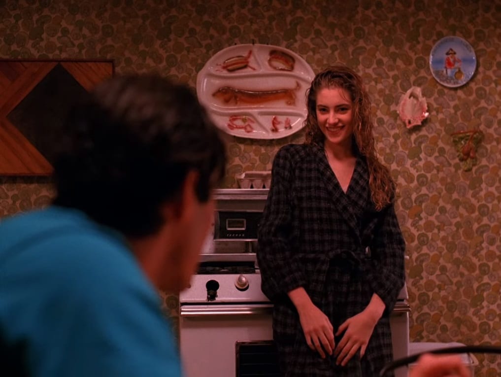 Shelly Johnson serves Bobby Briggs breakfast in front of a decorative platter featuring a dachshund on the set of Twin Peaks.