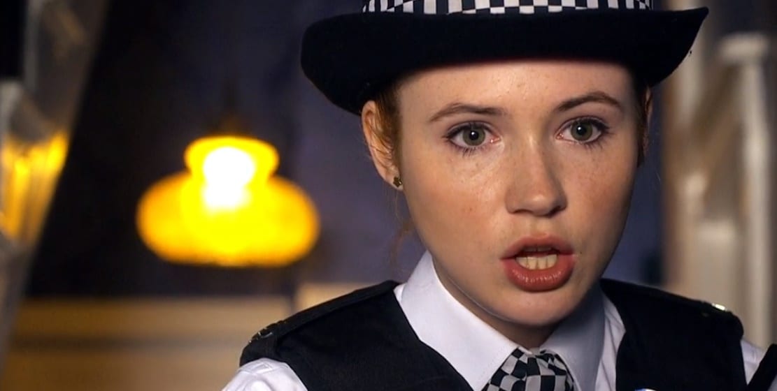 A close up of Amy Pond (Karen Gillan) in police uniform with a yellow lamp in the background