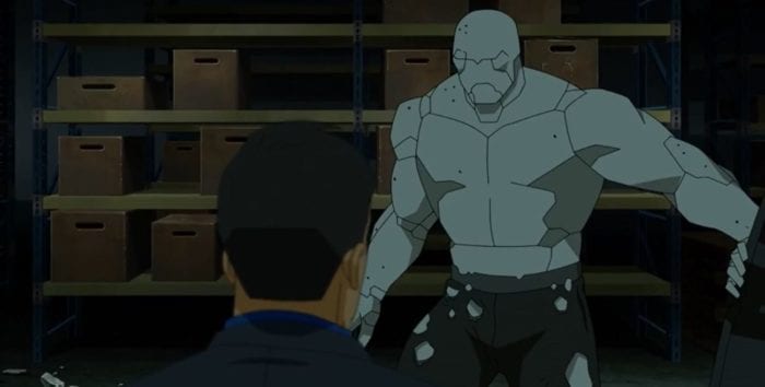 Titan stands in front of a member of a drug gang. Titan is encased in his rock armor and wearing sweatpants with bullet holes in them.