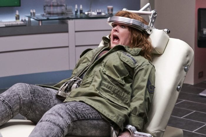 Lydia wails in surprise while confined to a chair by her head and hands.