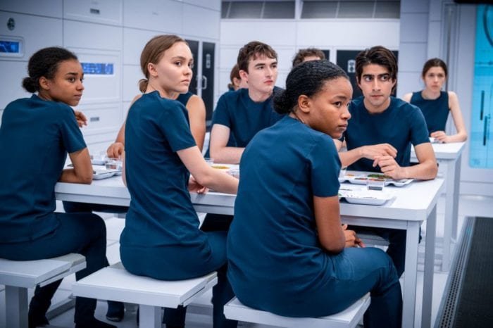 Sela and other crewmates turn to listen to a speaker.