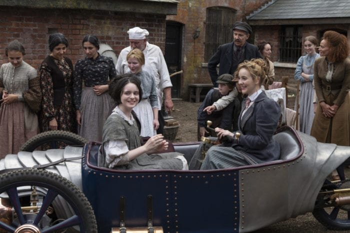 Penance and Myrtle sit in the small car surrounded by others looking on