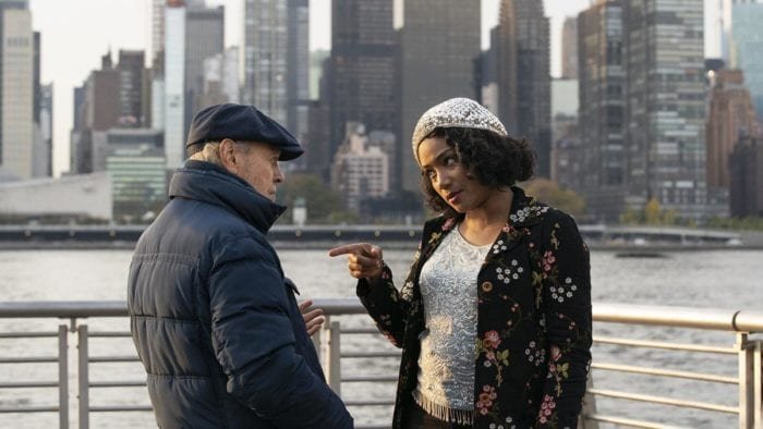 Emma points at Charlie in conversation by the river.