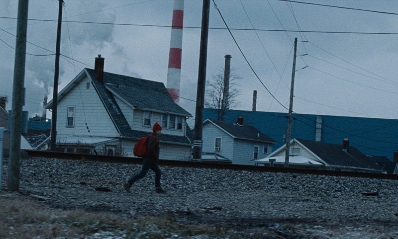 In this image from Nicole Riegel's Holler, Ruth (Jessica Barden) walks along a railroad rack in front of houses in her Ohio hometown.