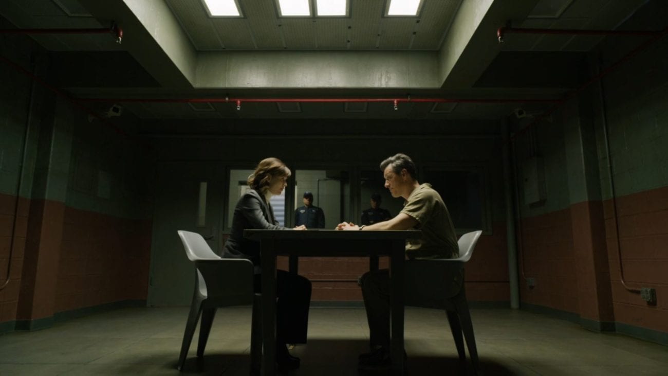 Kristen and a suspect face each other across a table in an interrogation room.