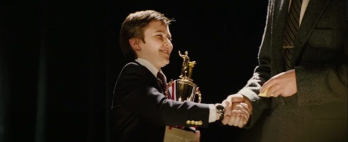 Joey (Cameron Bright) smiling and holding a trophy, shakes hands with a man in a suit