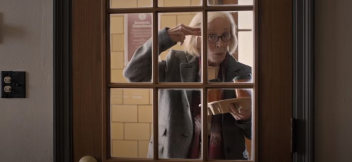 Professor Joan Hambling (Holland Taylor) looking through windows in a door while holding coffee