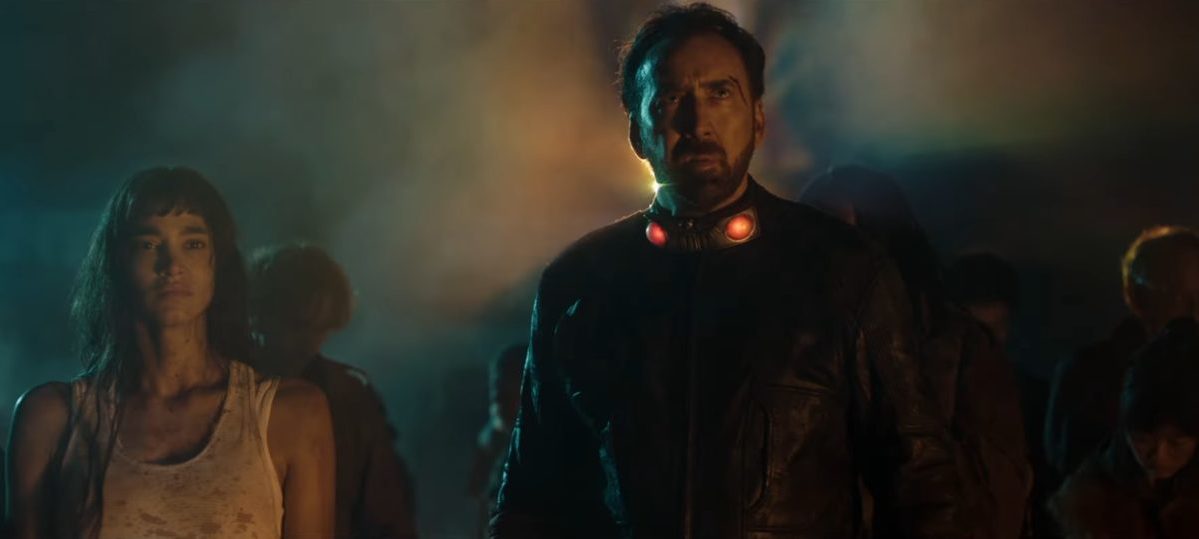 Sofia Boutella stands beside Nicolas Cage against a foggy background