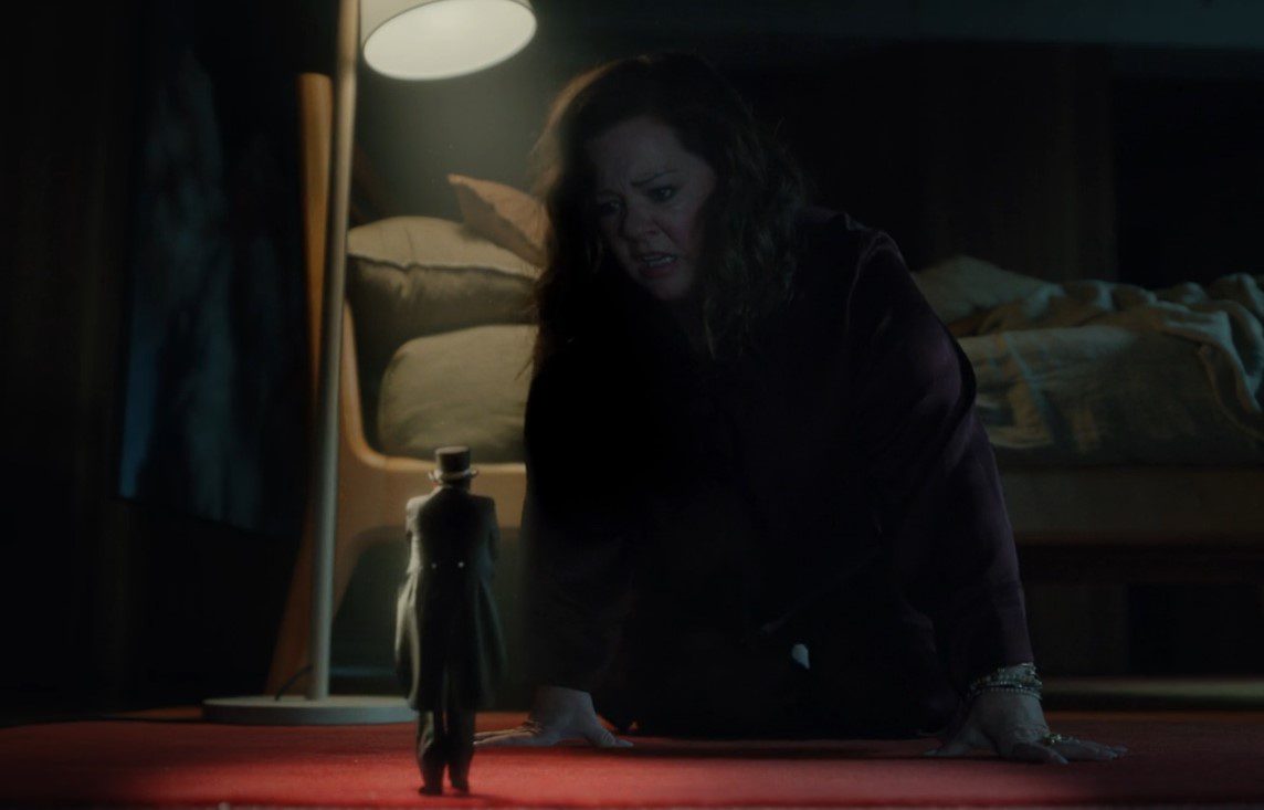 Frances (Melissa McCarthy) sits hunched over on the floor, staring down at a toy-sized Paul Drabb.
