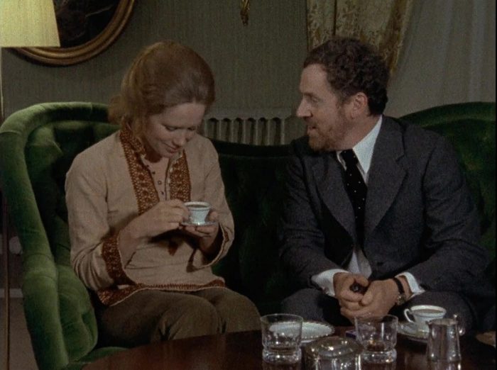 In this image from Episode 4 of Bergman's Scenes from a Marriage, “The Vale of Tears,” a thirsty Johan (Erland Josephson) is depicted on a green loveseat looking at Marianne (Liv Ullmann) as she holds a coffee cup.. 