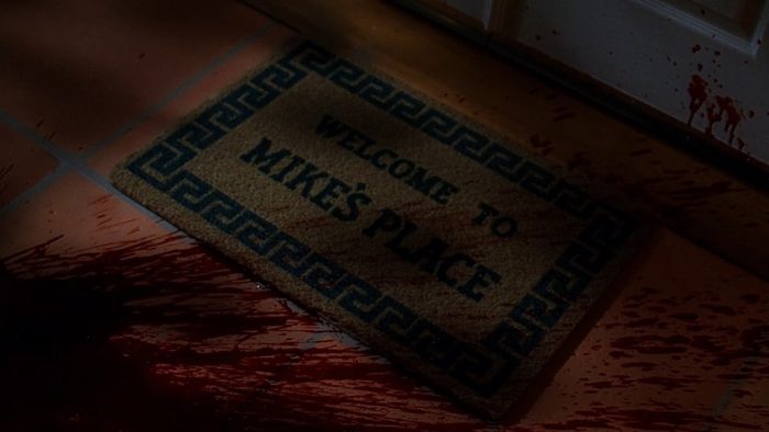 A splatter of blood over a doormat that reads 'Welcome to Mike's Place'