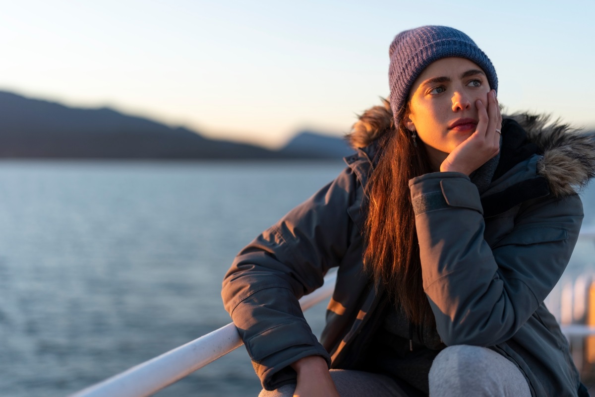 In this image from Maid, Alex (Margaret Qualley) is depicted on a ferry, wearing a winter jacket and knit cap, looking pensively off screen with the shore in the background.