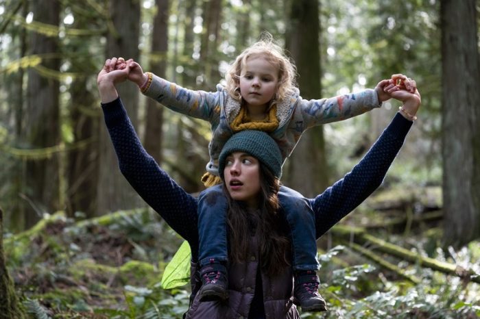 In this image from Maid, Alex (Margaret Qualley) carries Maddy (Rylea Nevaeh Whittet) on her back in the woods.