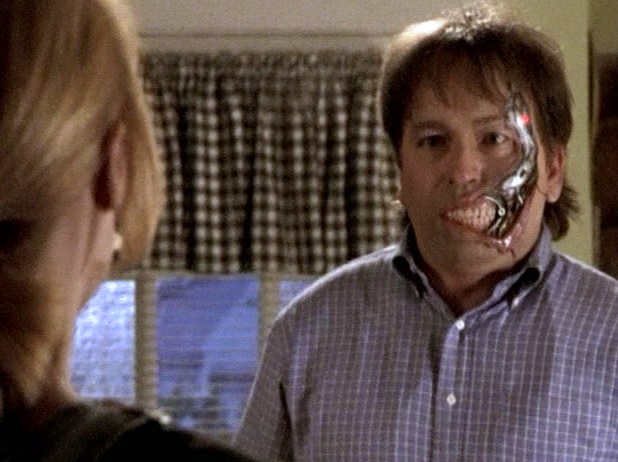 Ted Buchanan the robot with his metal underneath exposed in part of his face, confronting Buffy