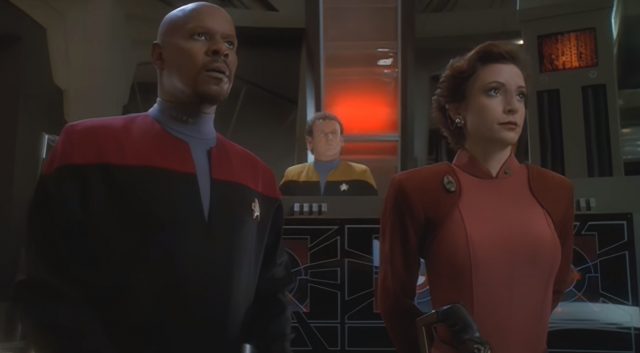 Captain Sisko and Major Kira wait for someone to transport aboard, while O'Brien stands behind his console in the background.