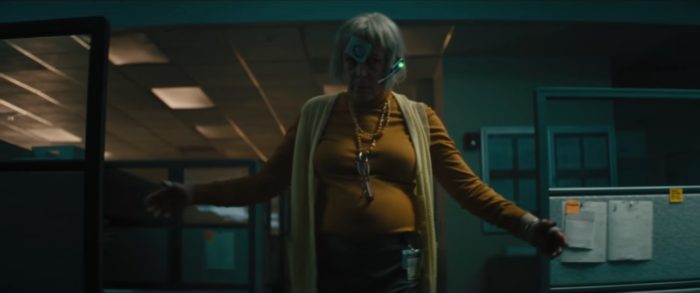 Jamie Lee Curtis appears threatinging in a tight-fitting mustard top and lemon hued sweater vest against an obvious fat-suit while wearing a post-it note with a circle on it on her forehead in Everything Everywhere All at Once