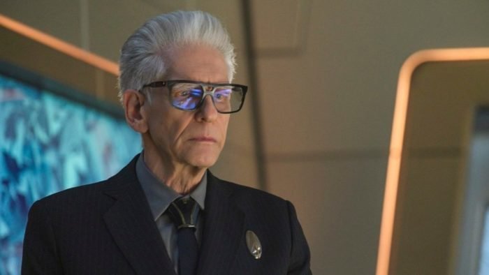 Kovich (David Cronenberg) stands in Culber's study looking surly