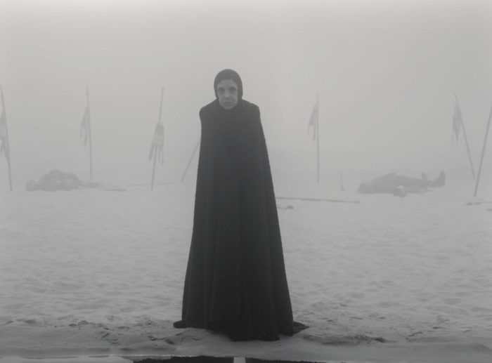A witch stands within the fog of an empty battlefield.
