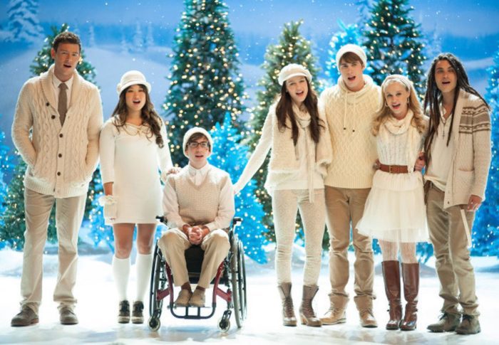 The cast of Glee in a winter scene with lit trees behind them in Glee, Actually