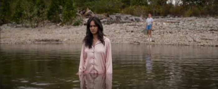Lottie stands in the lake waist deep with a bemused look on her face, as Jackie looks on from the shore in the background